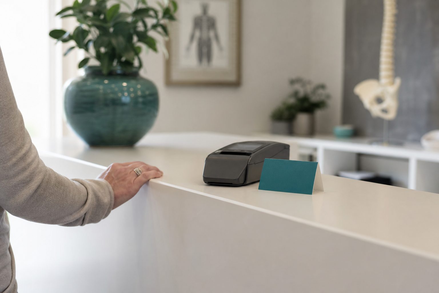 Bone white chiropractic reception counter with a slate card reader and a teal appointment card in soft daylight